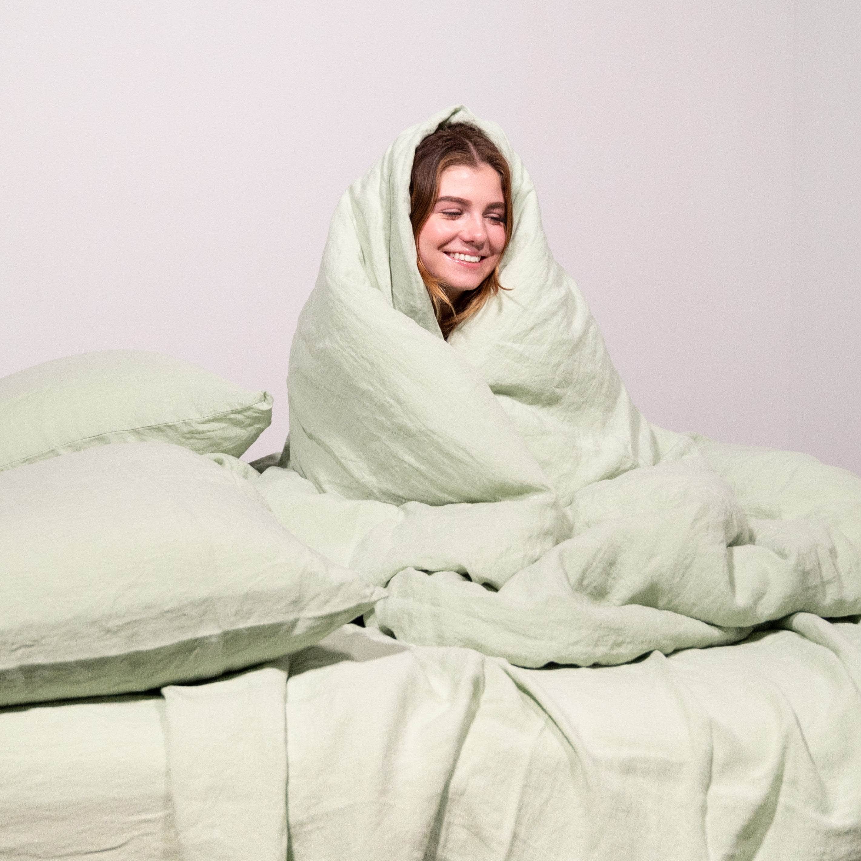 Girl wrapped in seafoam linen duvet with 2 seafoam linen pillows