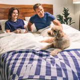 woman and man with dog sitting on white linen duvet cover and sheet set