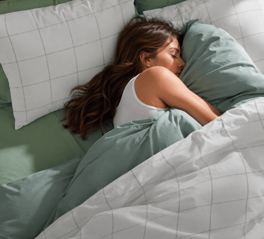 Woman lying in bed with green bedding and pillows