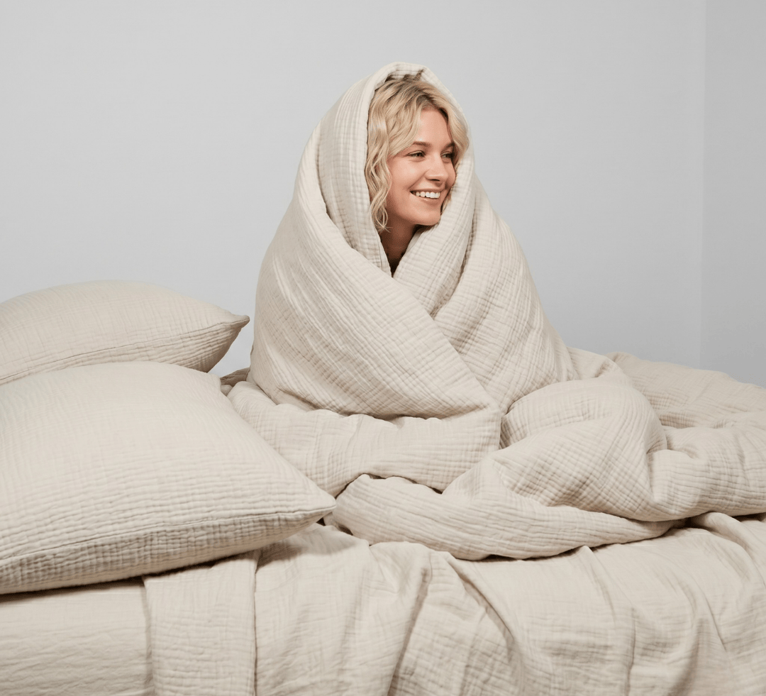 Person wrapped in a beige blanket on a bed with a plain background