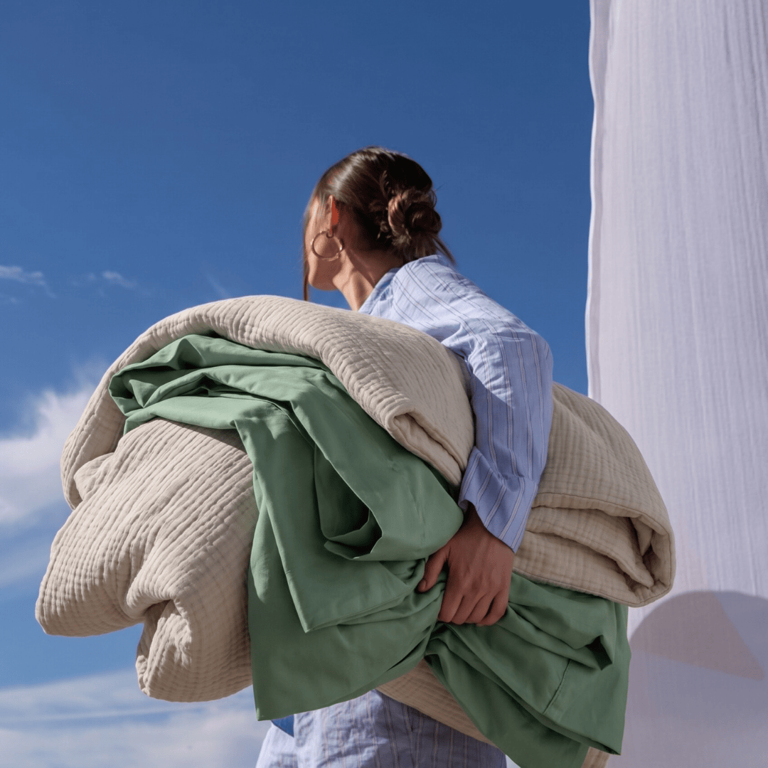 Person holding multiple blankets against a blue sky with white columns.