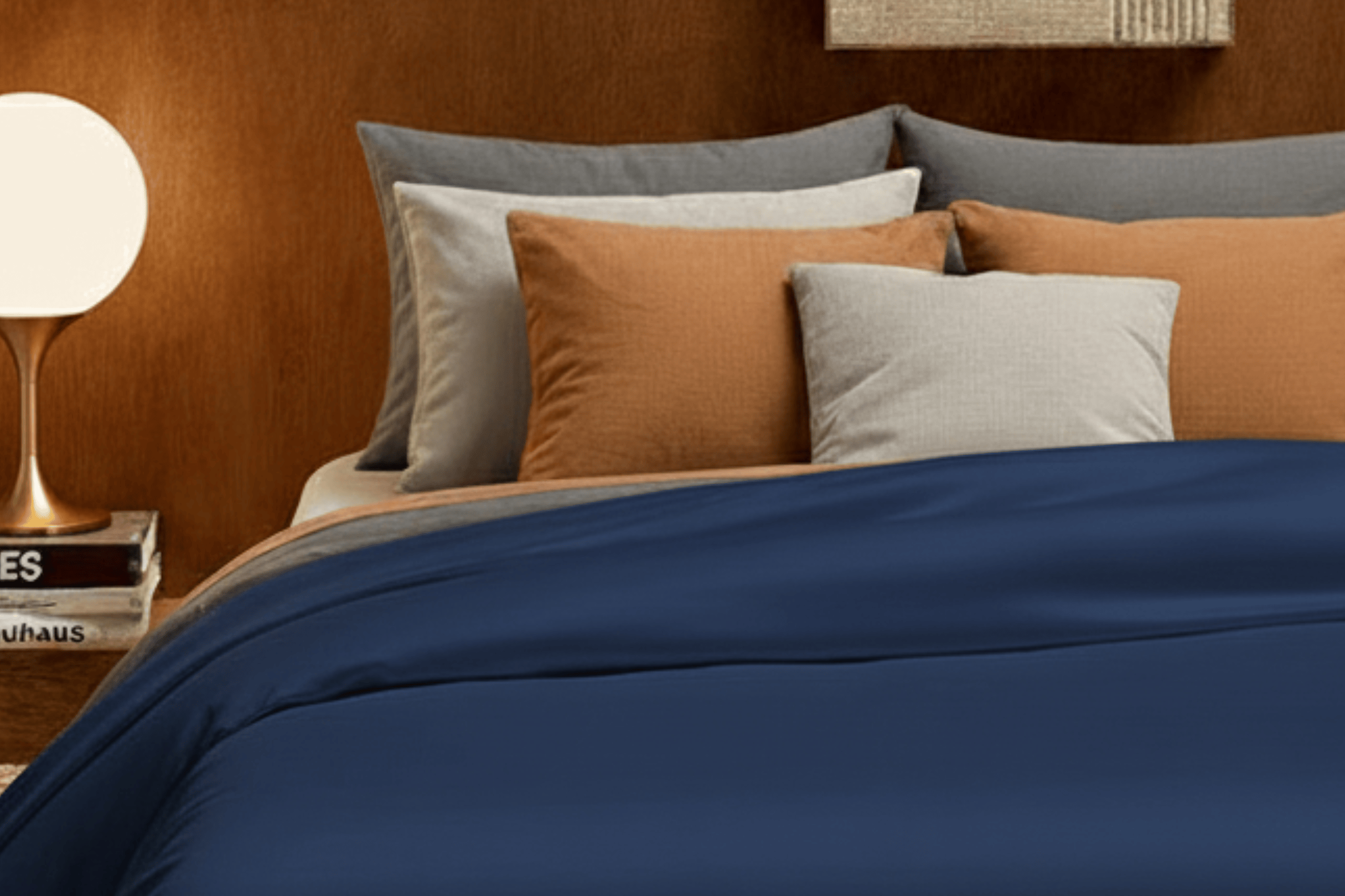 Bed with blue bedding and multicolored pillows against a brown wall with a decorative painting.