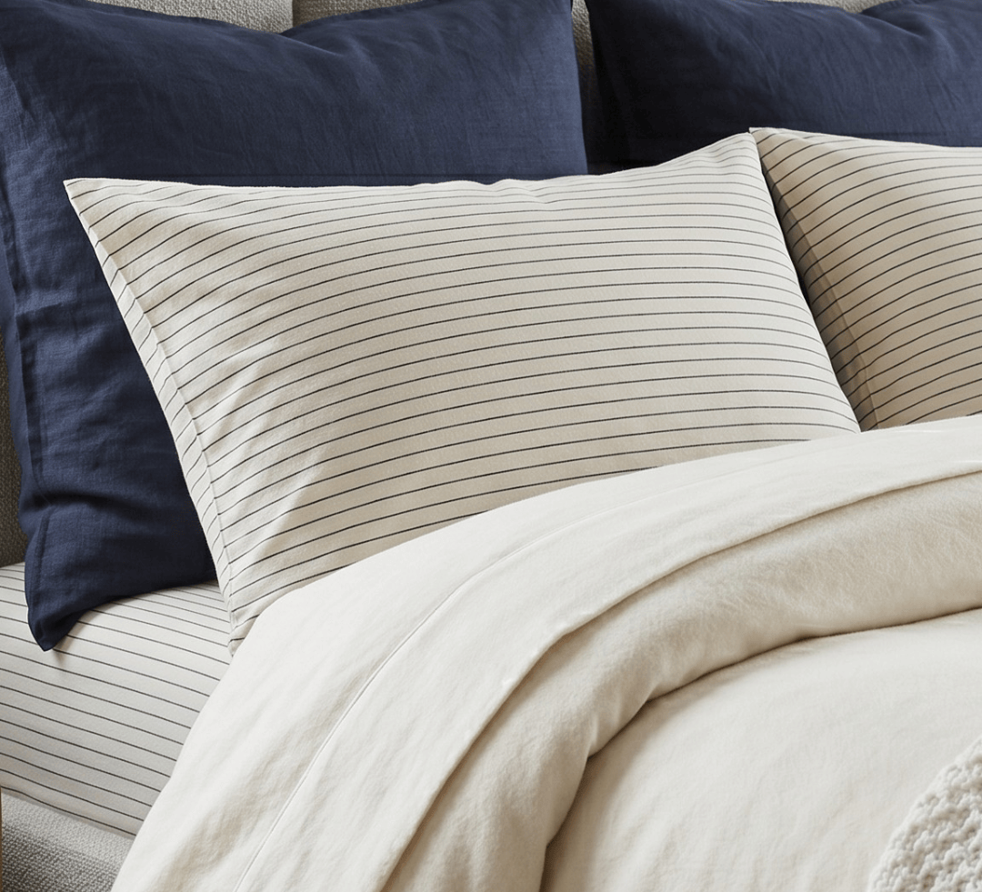 Neatly made bed with beige bedding and navy pillows against a neutral wall.