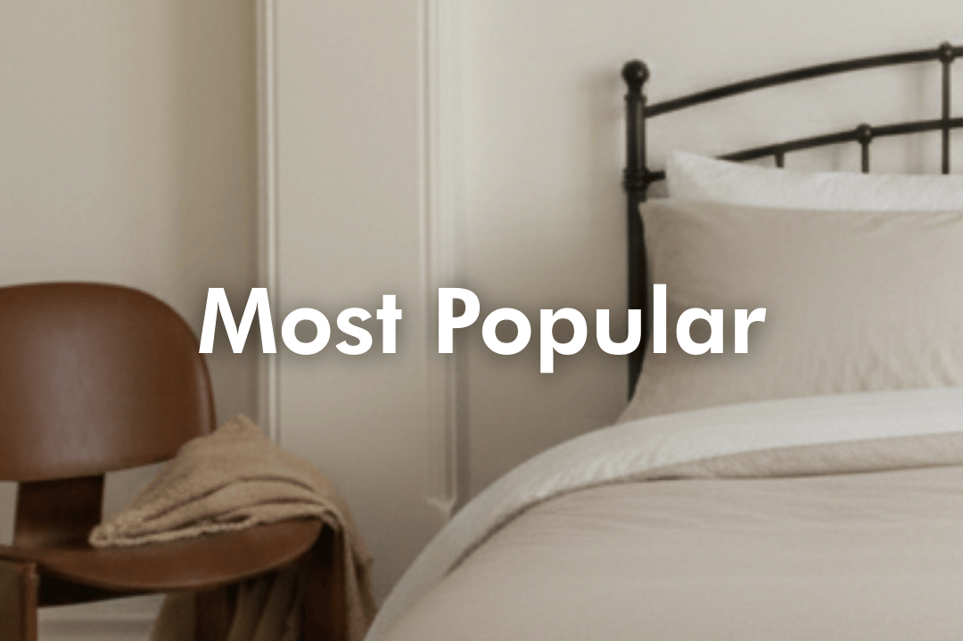 Neatly made bed with beige bedding and a brown chair in a bedroom setting.