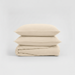 Beige bedding set with two pillows and a folded sheet on a light gray background