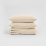 Beige bedding set with two pillows and a folded sheet on a light gray background
