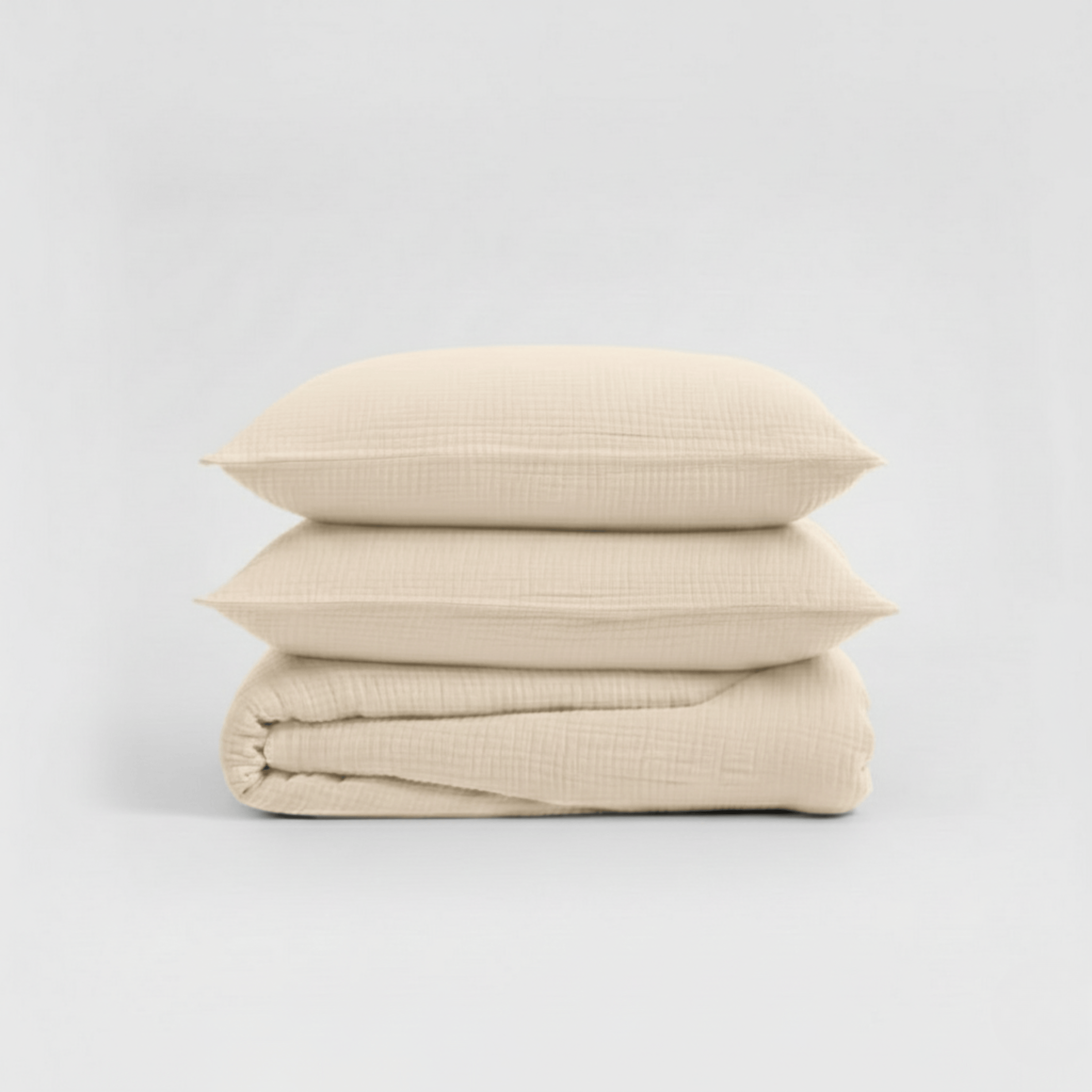 Beige bedding set with two pillows and a folded sheet on a light gray background