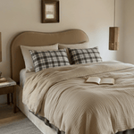 Neatly made bed with beige bedding and plaid pillows in a bedroom setting.