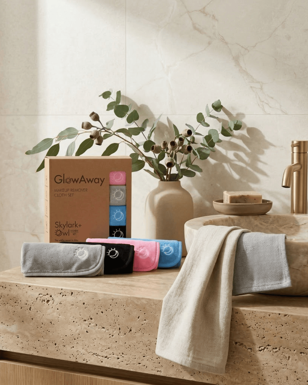 Bathroom setting with towels, a plant, and a box labeled 'GlowAway' on a marble countertop.