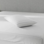 Image of a pillow protector on top of a gray bed with just a mattress protector on it