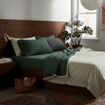 Bedroom with a wooden headboard, green bedding, and a plant near a window.