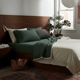 Bedroom with a wooden headboard, green bedding, and a plant near a window.
