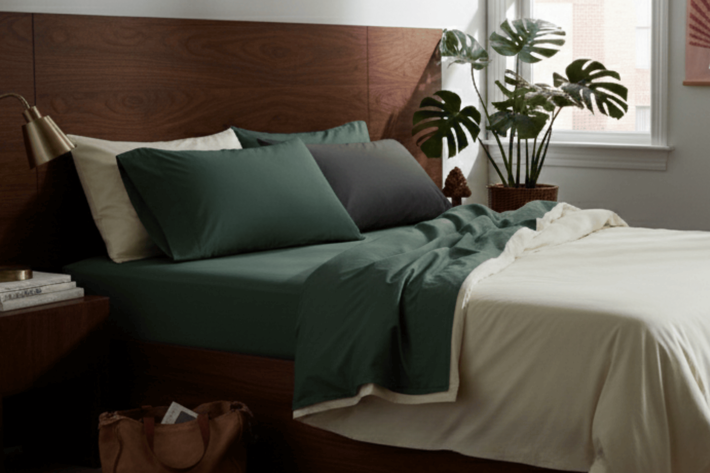 Bedroom with a wooden headboard, green bedding, and a plant near a window.