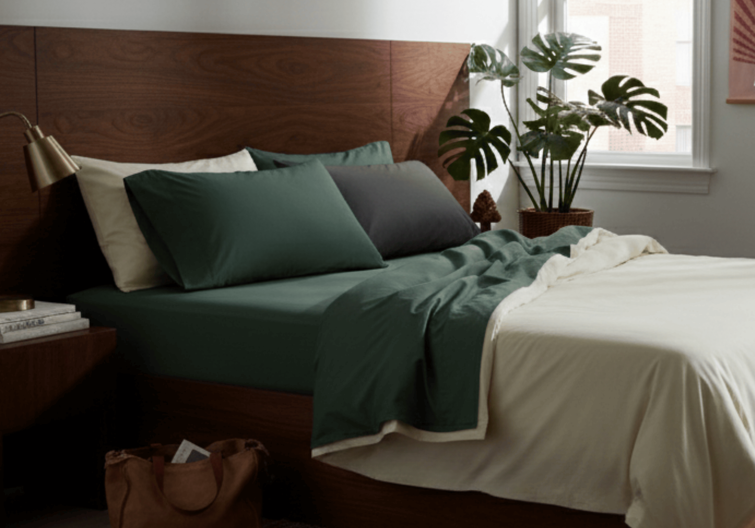 Bedroom with a wooden headboard, green bedding, and a plant near a window.