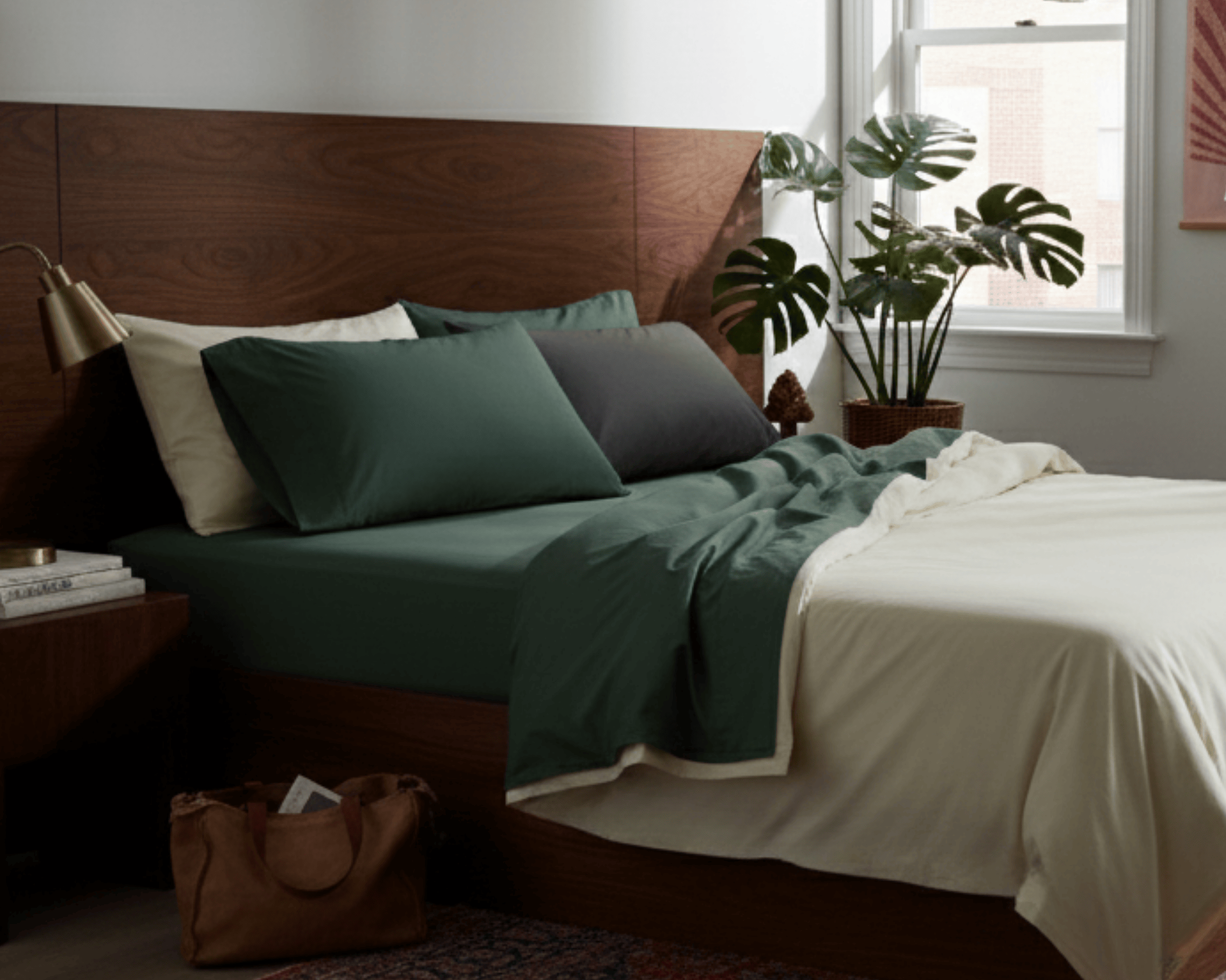 Bedroom with a wooden headboard, green bedding, and a plant near a window.