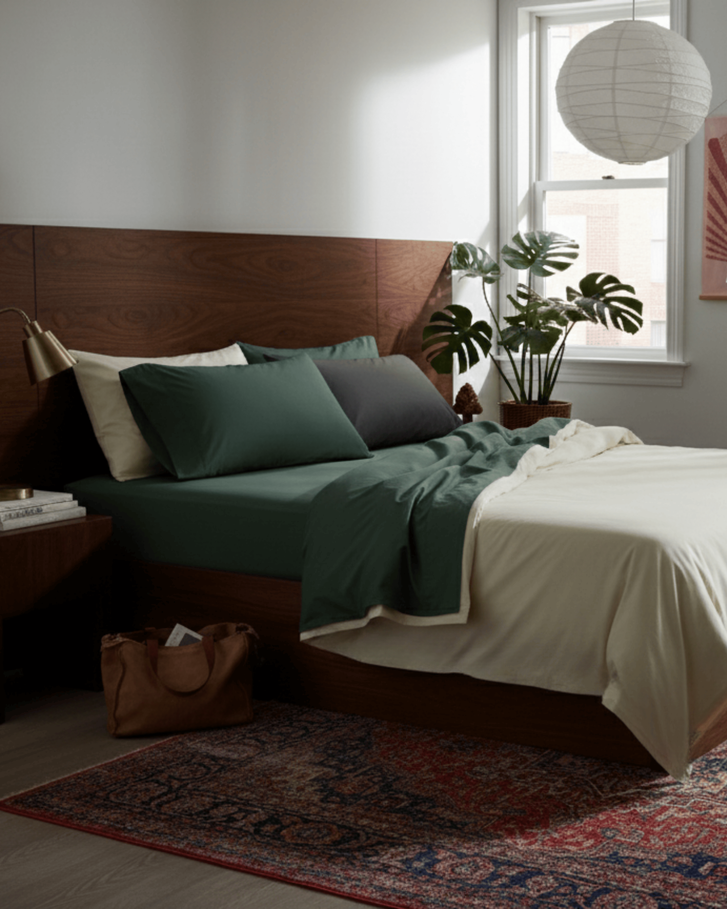 Bedroom with a wooden headboard, green bedding, and a plant near a window.