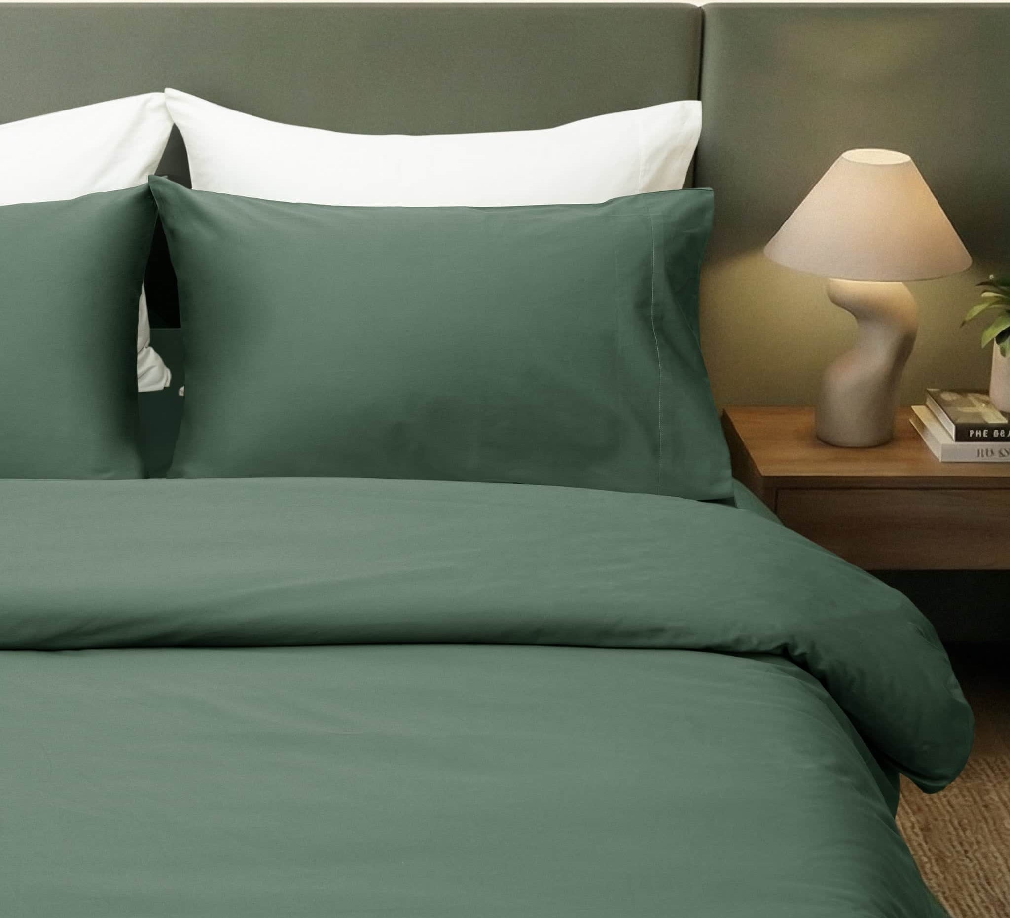 Green bedding set on a bed with a nightstand and lamp in the background.