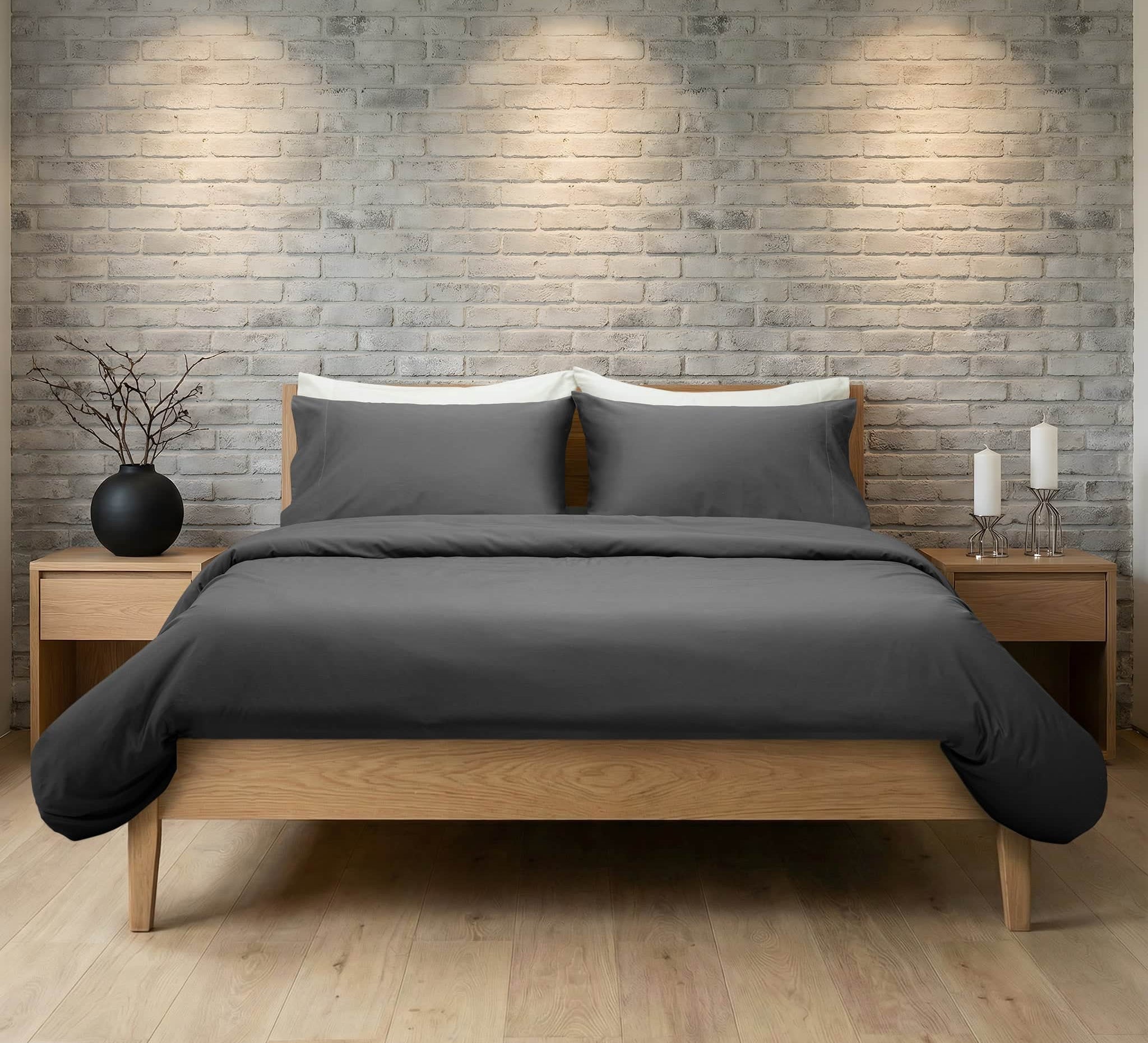 Bed with gray bedding and wooden frame against a brick wall.