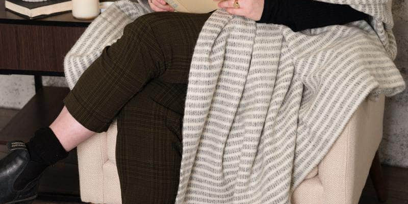 Woman reading in an armchair wrapped in a striped lambswool blanket