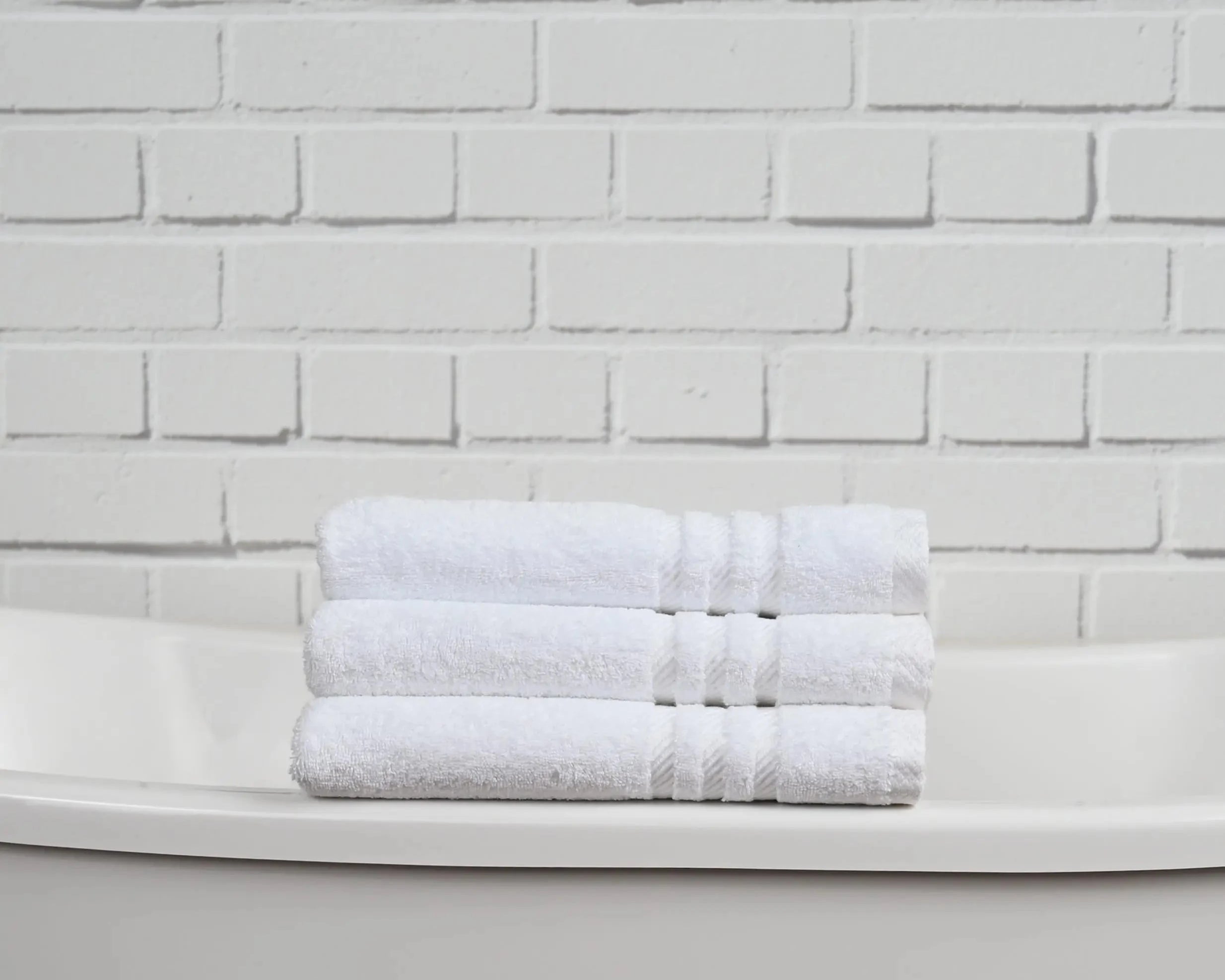 Stack of white towels on a white surface with a white brick wall background