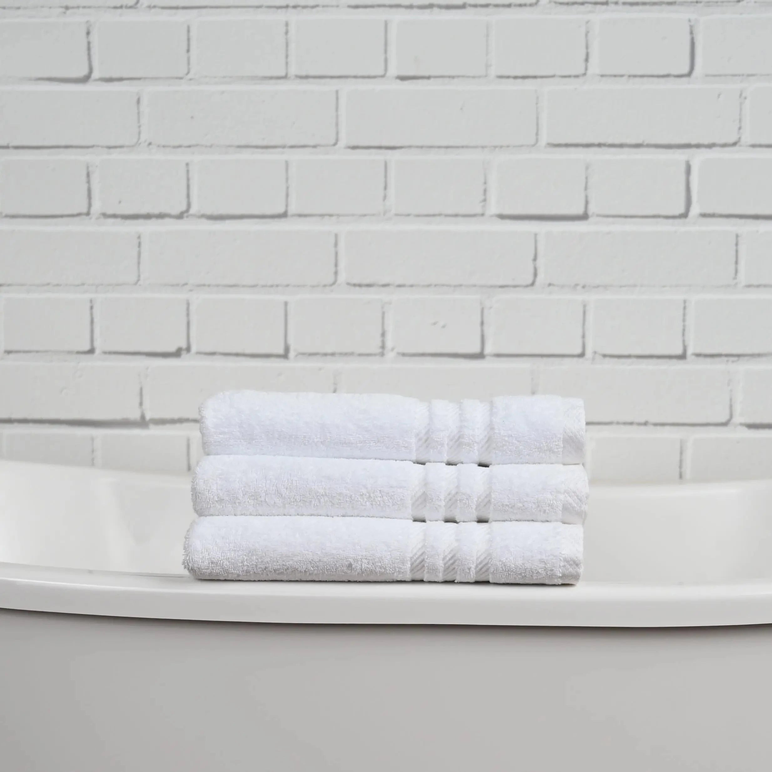 Stack of white towels on a white surface with a white brick wall background
