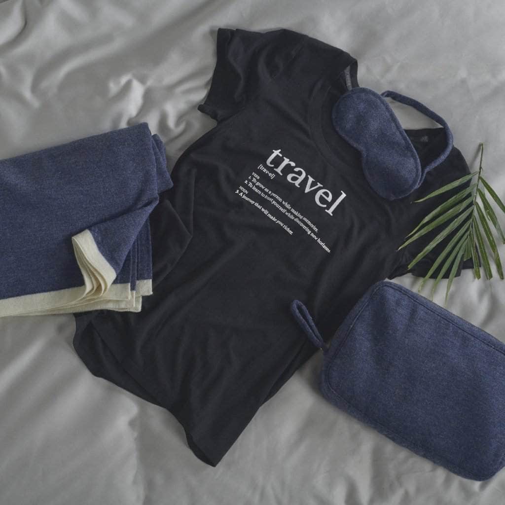 Flat lay of a black graphic tee with the Merino Wool Travel Set in Navy which includes an Eye Mask, a Blanket and a Travel Case