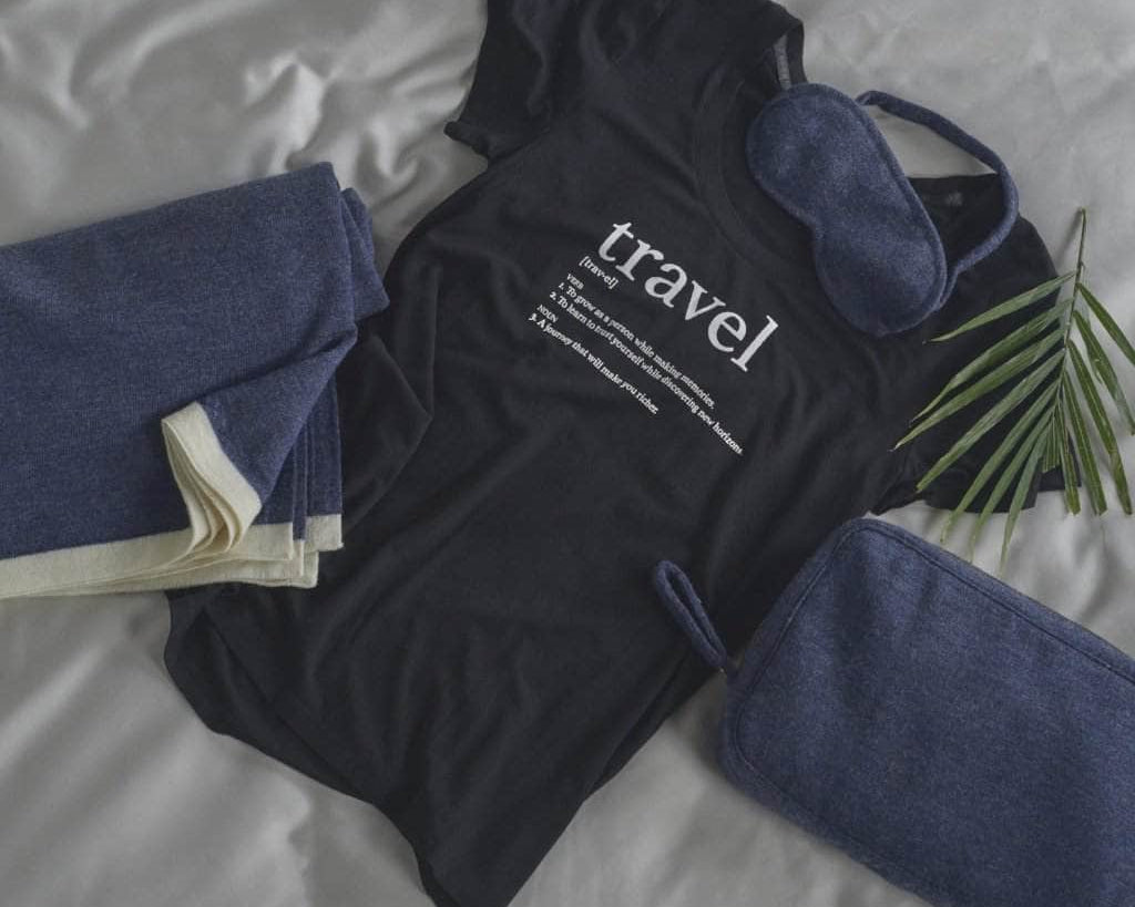 Flat lay of a black graphic tee with the Merino Wool Travel Set in Navy which includes an Eye Mask, a Blanket and a Travel Case