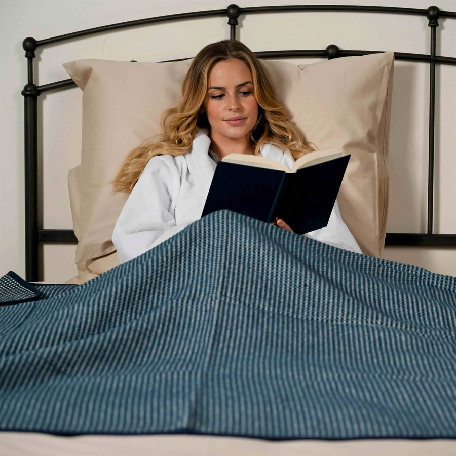 Woman reading a book on a bed with the Sapphire Alpine brushed cotton blanket on her