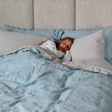 Woman sleeping in bed featuring Linen Duvet Cover in Blue Mist and Linen Sheet Set in Mushroom