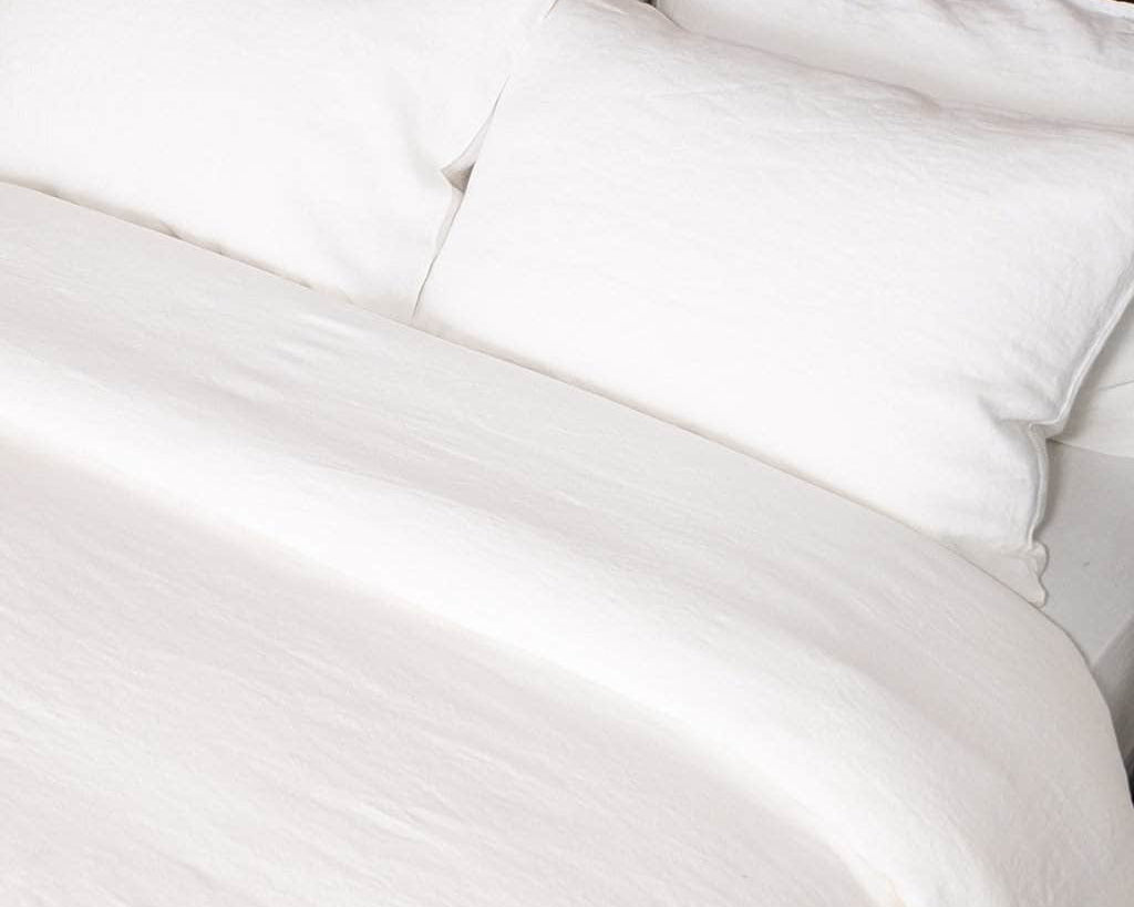 close up of bed with white linen duvet and white linen sheet set