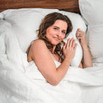 woman laying in white linen sheet set and  white linen duvet cover