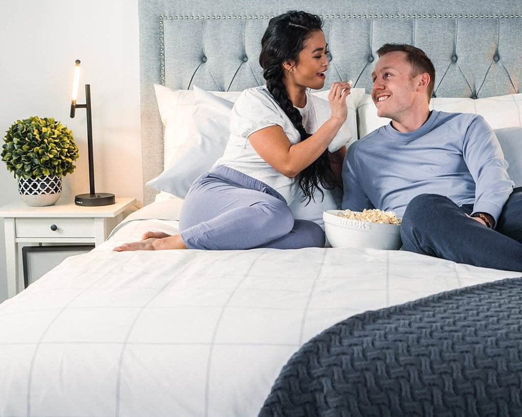 Couple enjoying popcorn in bed featuring the Essential Collection Percale Sheet Set in Light Grey Frame