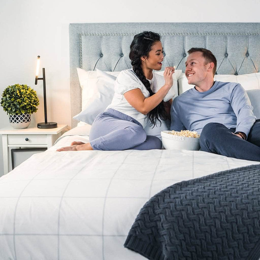 Couple enjoying popcorn in bed featuring the Essential Collection Percale Sheet Set in Light Grey Frame
